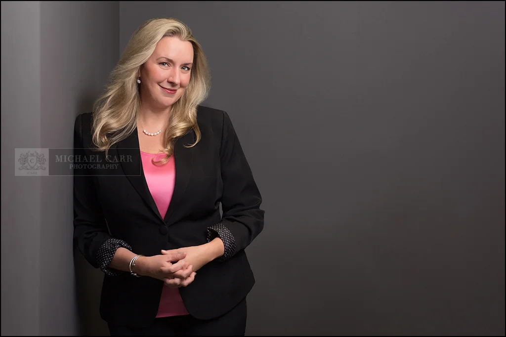 Professional branding portrait of an attorney standing against a modern gray studio background.