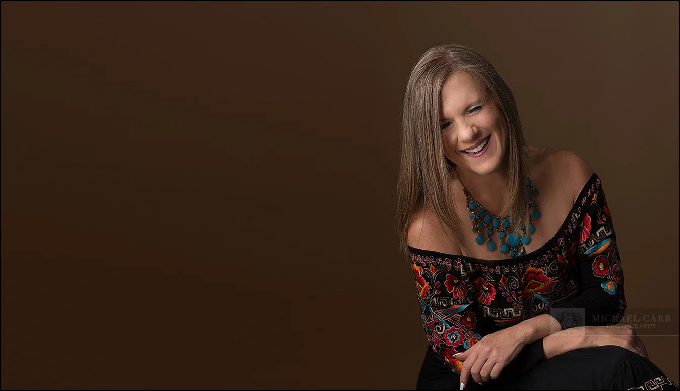 Lifestyle branding portrait of a creative professional smiling against a warm brown background.