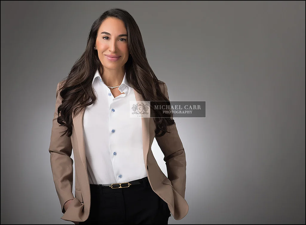 Professional business portrait of a Houston businesswoman wearing a tan blazer and white shirt against a gray background.