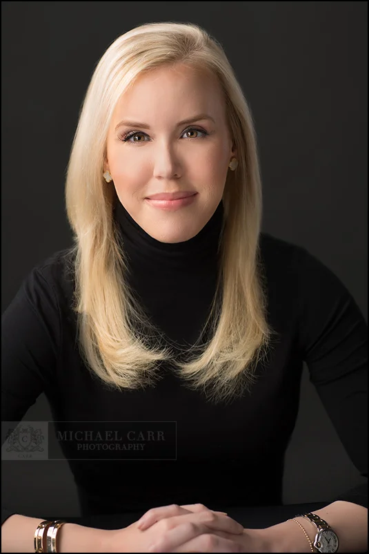 Professional headshot of a young Houston businesswoman wearing a black turtleneck against a gray background.