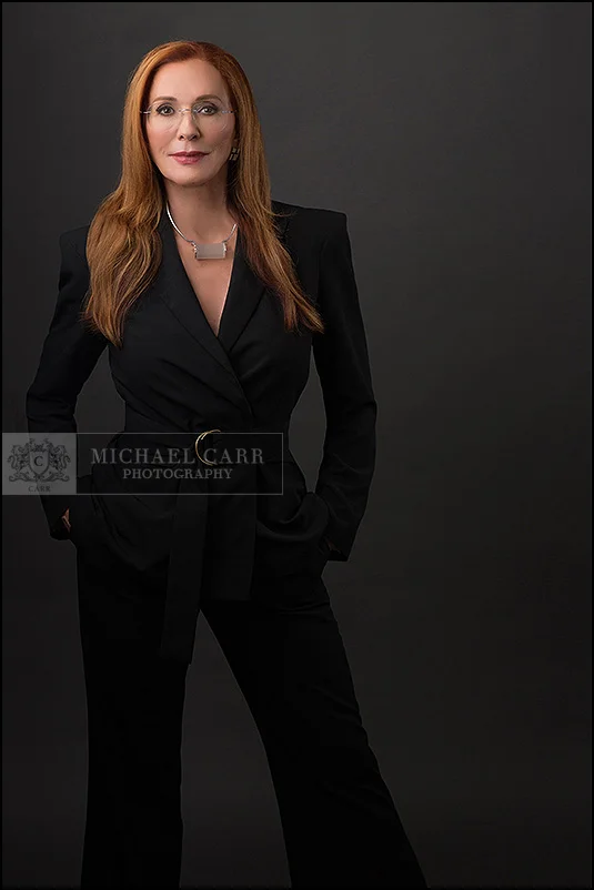 Professional headshot of a Houston businesswoman wearing a black pantsuit against a dark gray background.