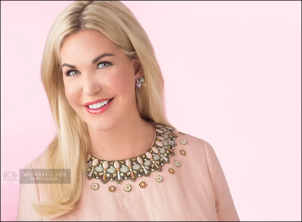 Professional beauty portrait of a Houston businesswoman wearing a statement necklace against a soft pink background.