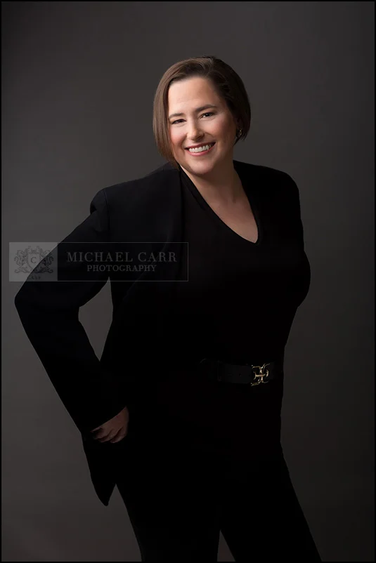 Personal Branding Photographer Relaxed portrait of a smiling professional woman in black attire against a clean gray studio background.